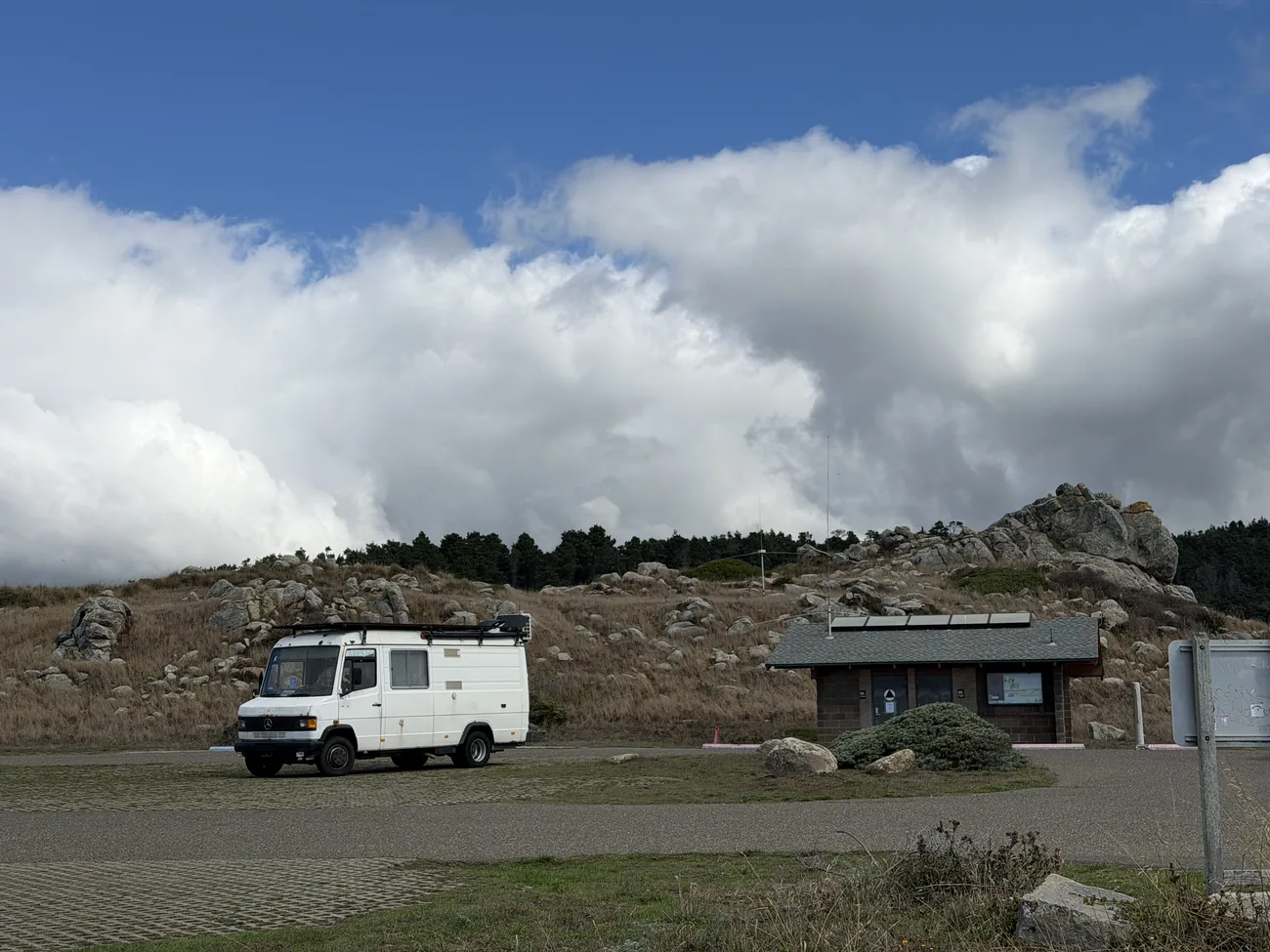 The van — a white 1991 Mercedes-Benz 609D — parked on a coastal bluff among rocks and windswept grass